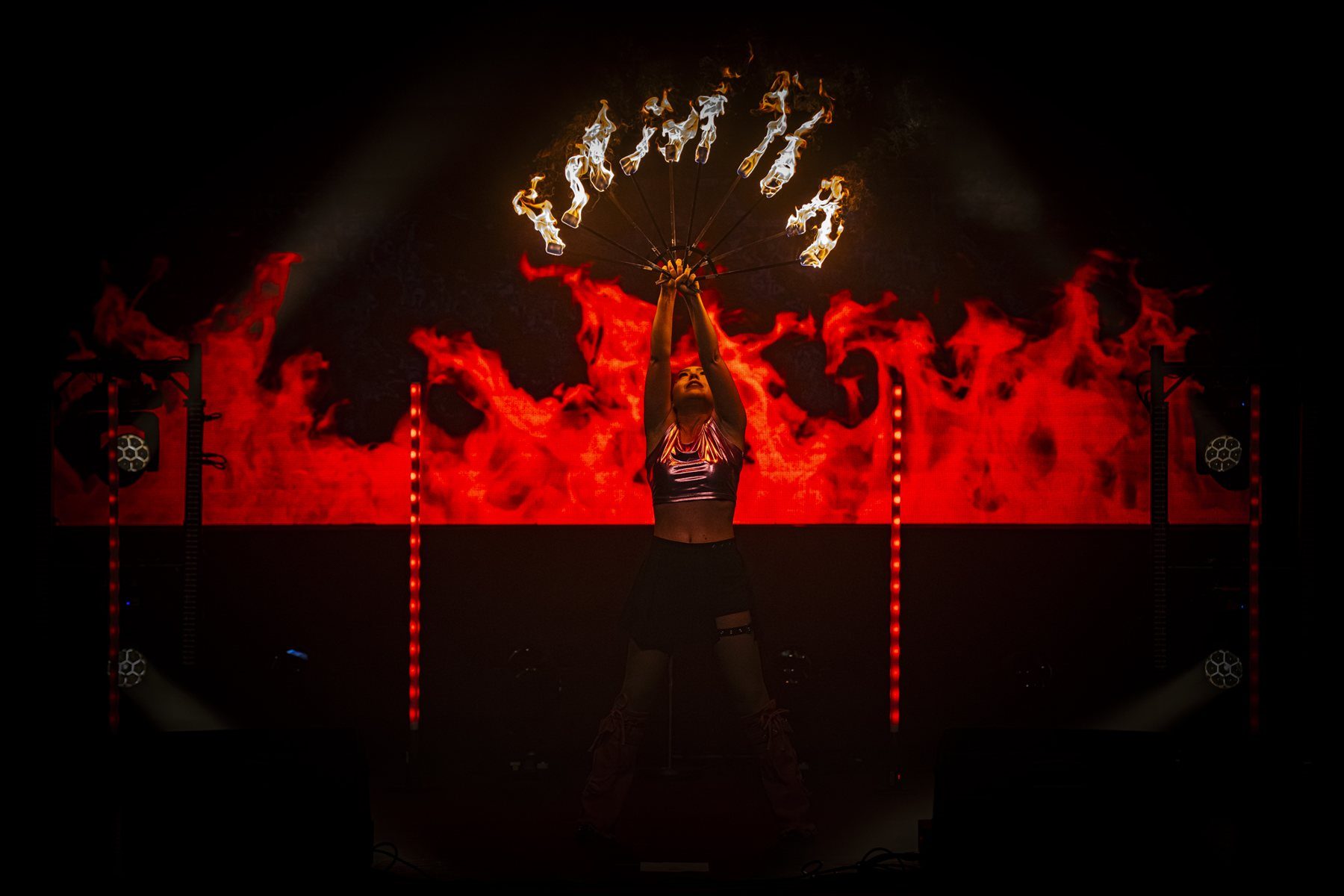 A K-Pop Fantasy performer raises a flaming fan in front of a wall of fire visuals