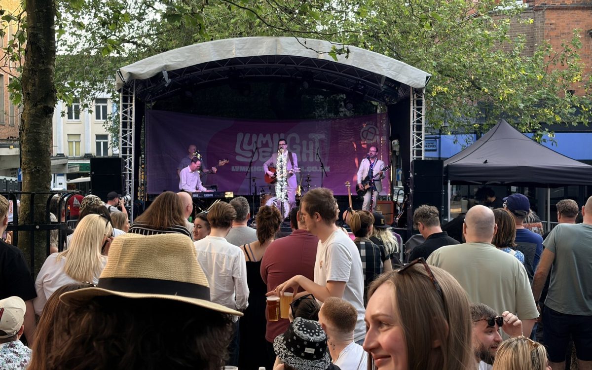 A busy crowd at tables in front of the Lymelight stage under the trees
